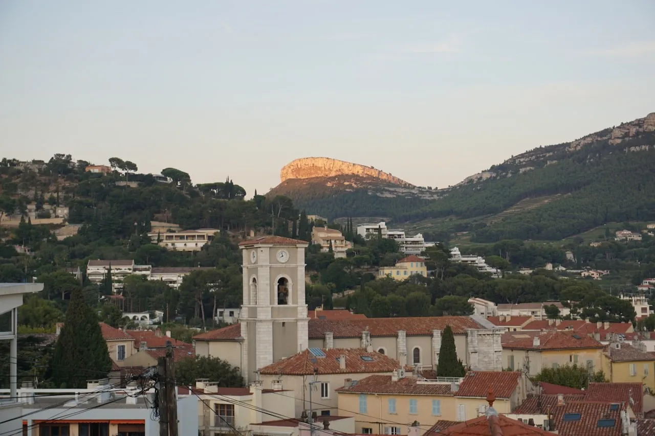 Bourg méditerranéen et son clocher au crépuscule, toits de tuiles et collines en arrière-plan.
